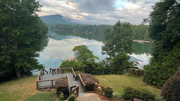 A patio area with a fire pit, seating, and a view of a lake surrounded by trees. - LAKE COTTAGE on deep water w/ incredible views! Hot tub/pool table/dock/kayaks (Blairsville)