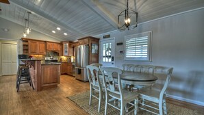 A spacious kitchen with wooden cabinets, a central island, and a dining area with white chairs. - LAKE COTTAGE on deep water w/ incredible views! Hot tub/pool table/dock/kayaks (Blairsville)