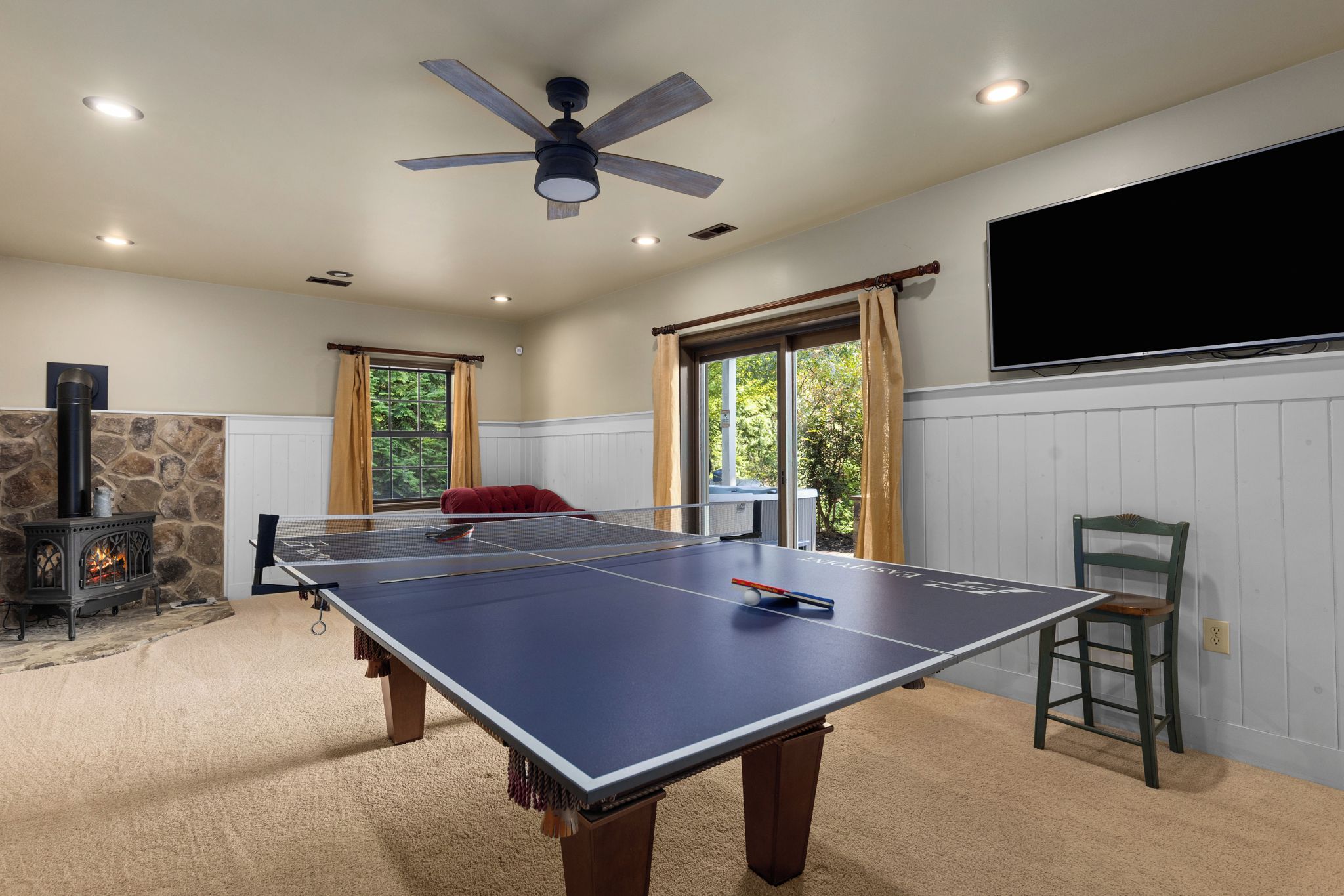 A room with a ping pong table, a fireplace, and a ceiling fan.