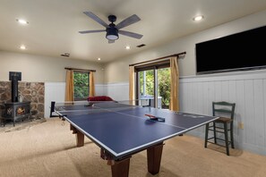 Una stanza con tavolo da ping pong, camino e ventilatore a soffitto.