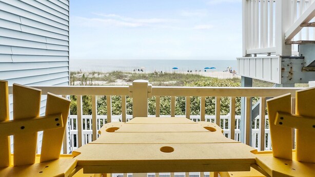 A balcony with a view of the beach, white railings, and yellow chairs. - Enjoy Sunset Views at Cozy Oceanfront Condo + Pool on Ocean Isle Beach, NC (Ocean Isle Beach)