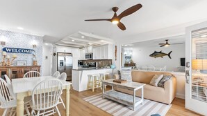 A spacious living area with a kitchen, dining table, and a sofa. - Enjoy Sunset Views at Cozy Oceanfront Condo + Pool on Ocean Isle Beach, NC (Ocean Isle Beach)