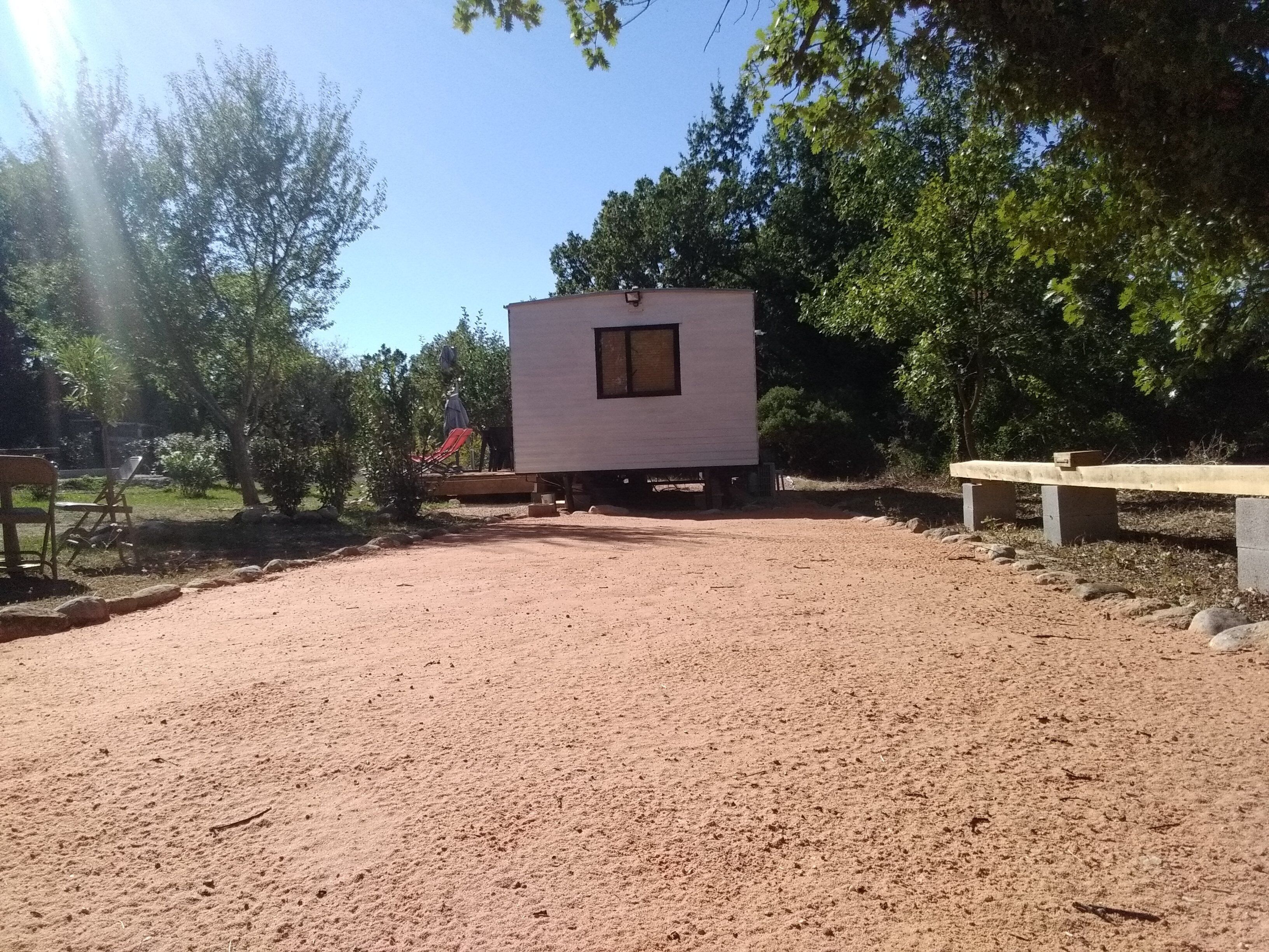 A small, single-story building with a window, surrounded by trees and a gravel area.