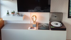 A modern living room with a flat-screen TV mounted on the wall, a built-in shelf with decorative items, a record player, and a light fixture. - Quiet and very few neighbors around (Riez)