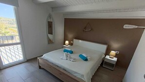 Une chambre à coucher avec un grand lit, deux tables de chevet avec des lampes, un miroir et une vue sur l’extérieur.