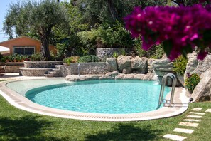 Una piscina con bordo in pietra, circondata da un prato curato e diverse piante.
