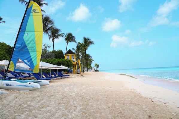 A beach with lounge chairs, a sailboat, and a yellow building. - Private Pool, 3 mins from Beach - Turtle View 2 (Porters)
