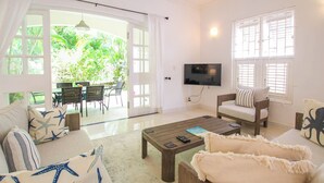 A spacious living room with a large TV, comfortable seating, and a view of a lush garden through the glass doors. - Private Pool, 3 mins from Beach - Turtle View 2 (Porters)