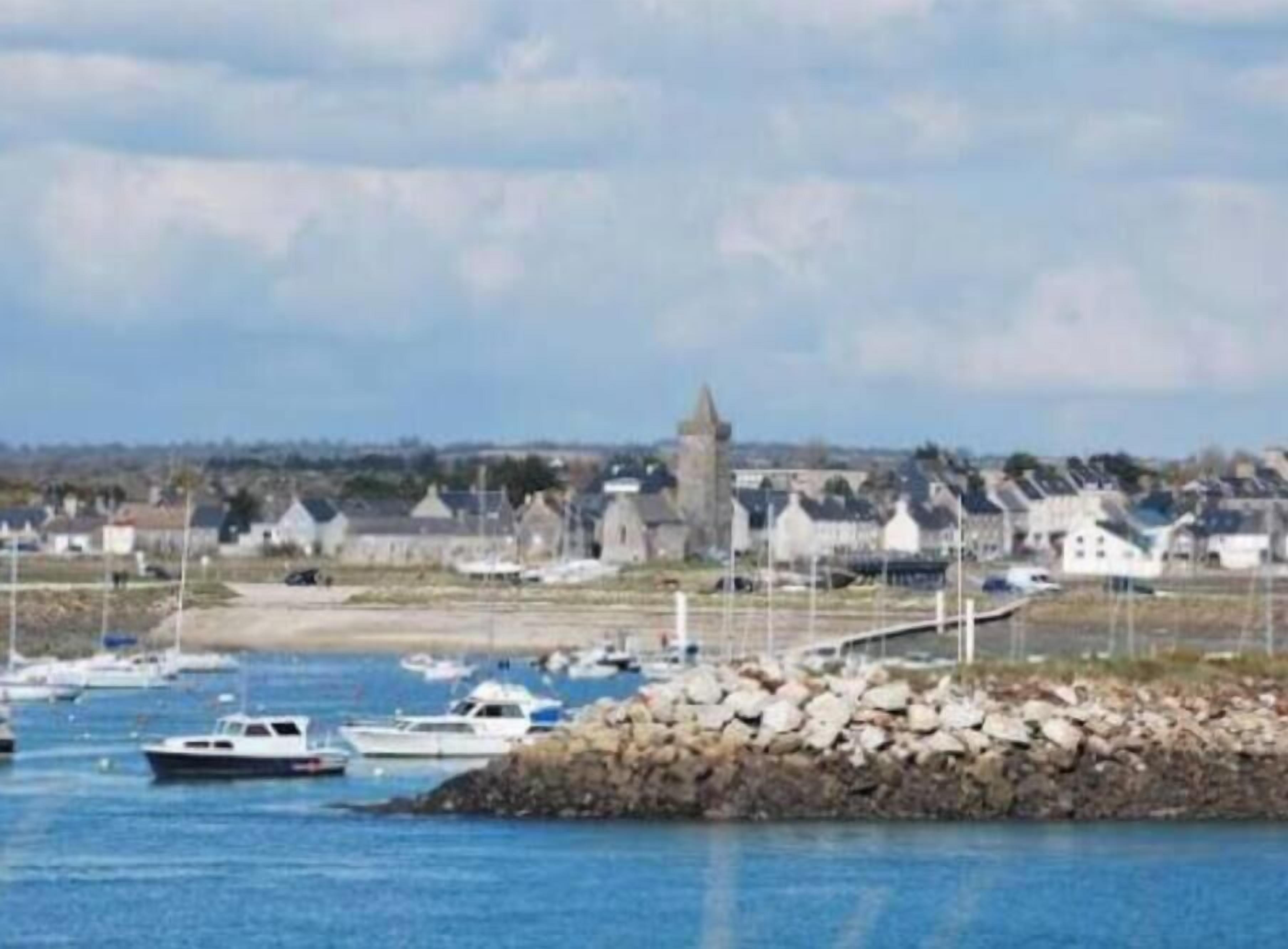 A coastal town with a prominent tower, boats in the water, and a rocky shoreline.