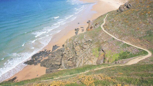 A coastal landscape with a sandy beach, rocky cliffs, and a winding path.