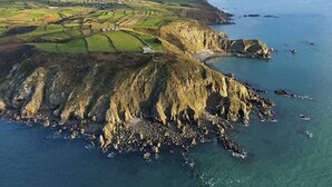 An aerial view of a coastal area with terraced fields, rocky cliffs, and a small beach.