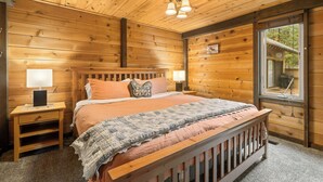 A wooden cabin bedroom with a bed, two bedside tables, a window, and a ceiling light fixture. - Quintessential Cabin in Sunriver's Best Location  - Cluster Cabin #2 (Sunriver)