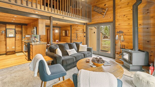A cabin interior with a loft bedroom, a kitchen, a living area with a sofa and coffee table, and a wood-burning stove. - Quintessential Cabin in Sunriver's Best Location  - Cluster Cabin #2 (Sunriver)