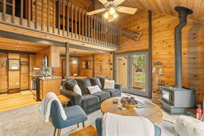 A cabin interior with a loft bedroom, a kitchen, a living area with a sofa and coffee table, and a wood-burning stove. - Quintessential Cabin in Sunriver's Best Location  - Cluster Cabin #2 (Sunriver)