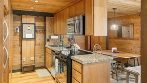 A wooden cabin interior with a kitchen featuring a stove, oven, refrigerator, and granite countertop. - Quintessential Cabin in Sunriver's Best Location  - Cluster Cabin #2 (Sunriver)