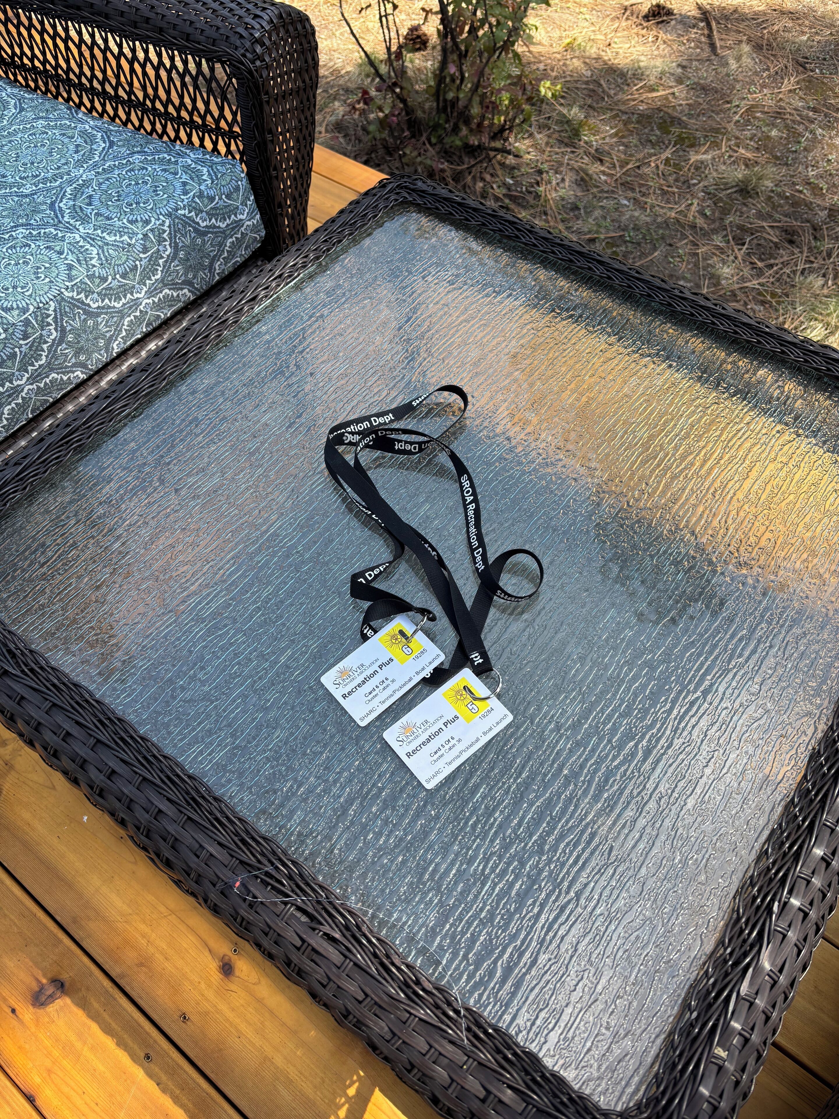 Een rieten stoel met een glazen tafeltje, twee lanyards met identiteitskaarten, en een houten terras.