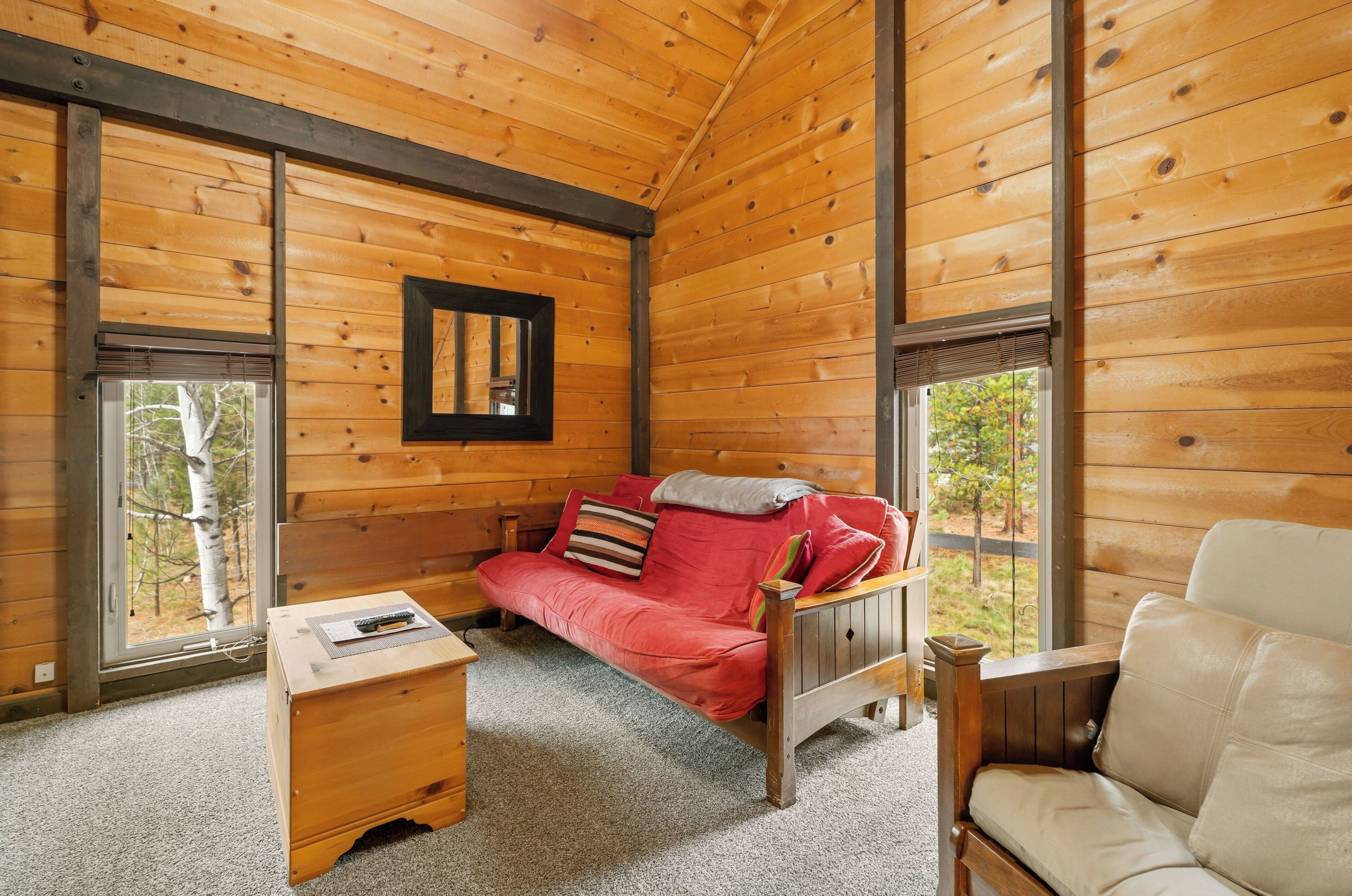 A wooden cabin interior with a red sofa, a beige armchair, and a small wooden table.