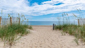 A sandy beach path leading to the ocean, flanked by wooden fences and tall grasses.