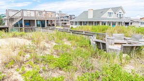 A beachfront property with a wooden deck, a covered outdoor area, and a house with a large window overlooking the beach.