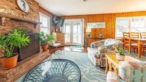 A cozy living room with a brick fireplace, comfortable seating, and a large window providing natural light.