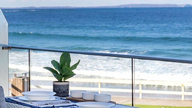 Ein Balkon mit Blick auf das Meer, einem Blumentopf und einem Tisch, der mit Tellern und Schüsseln gedeckt ist.