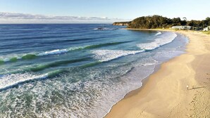 Ein Strand mit Wellen, einem sandigen Ufer und bewaldeter Landschaft im Hintergrund.