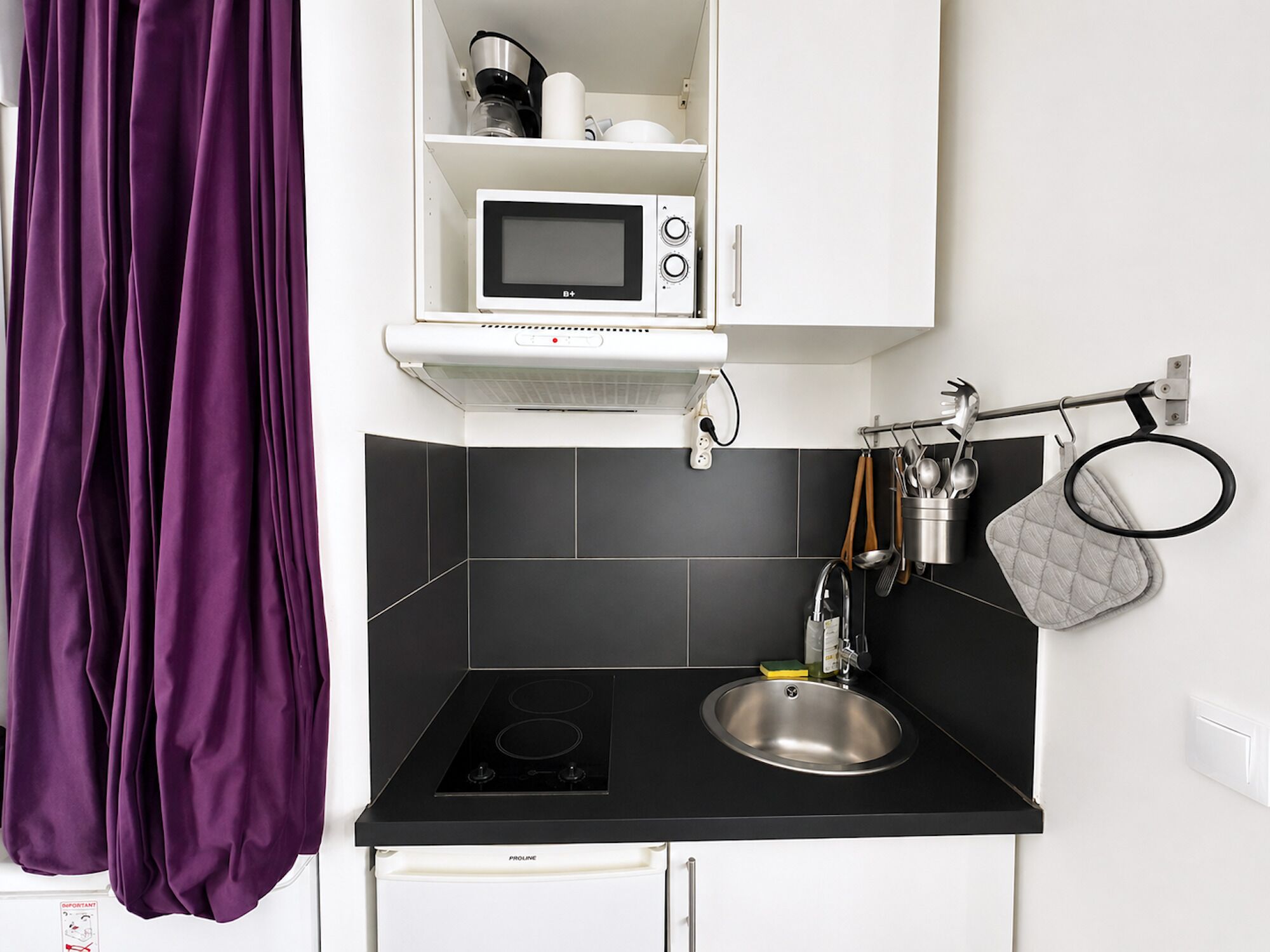 A modern kitchen with a black countertop, a stainless steel sink, a microwave, and a kettle on the shelf.