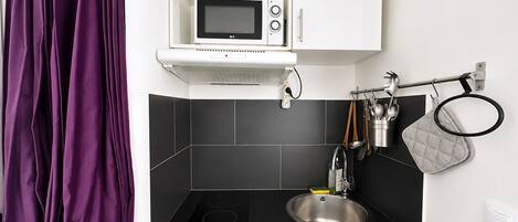 Una cocina moderna con encimera negra, pileta de acero inoxidable, microondas y tetera en la alacena.