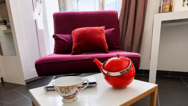Een moderne woonkamer met een rode bank, een witte bijzettafel, een rode theepot en een bloemenbeker.
