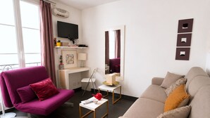 Een moderne woonkamer met een paarse fauteuil, een beige bank, een kleine witte tafel en een bureau met een computer en een flatscreen televisie.