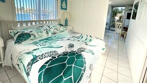 A bedroom with a large bed, a view of the sea through the window, a white wardrobe, and a small balcony area.