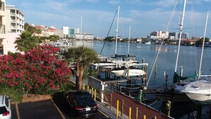 A marina with boats docked, a parking area, and buildings in the background.