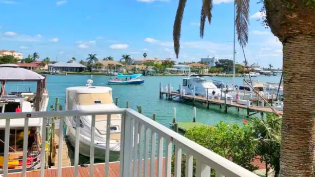A marina with boats docked, a clear blue sky, and a view of buildings in the background.