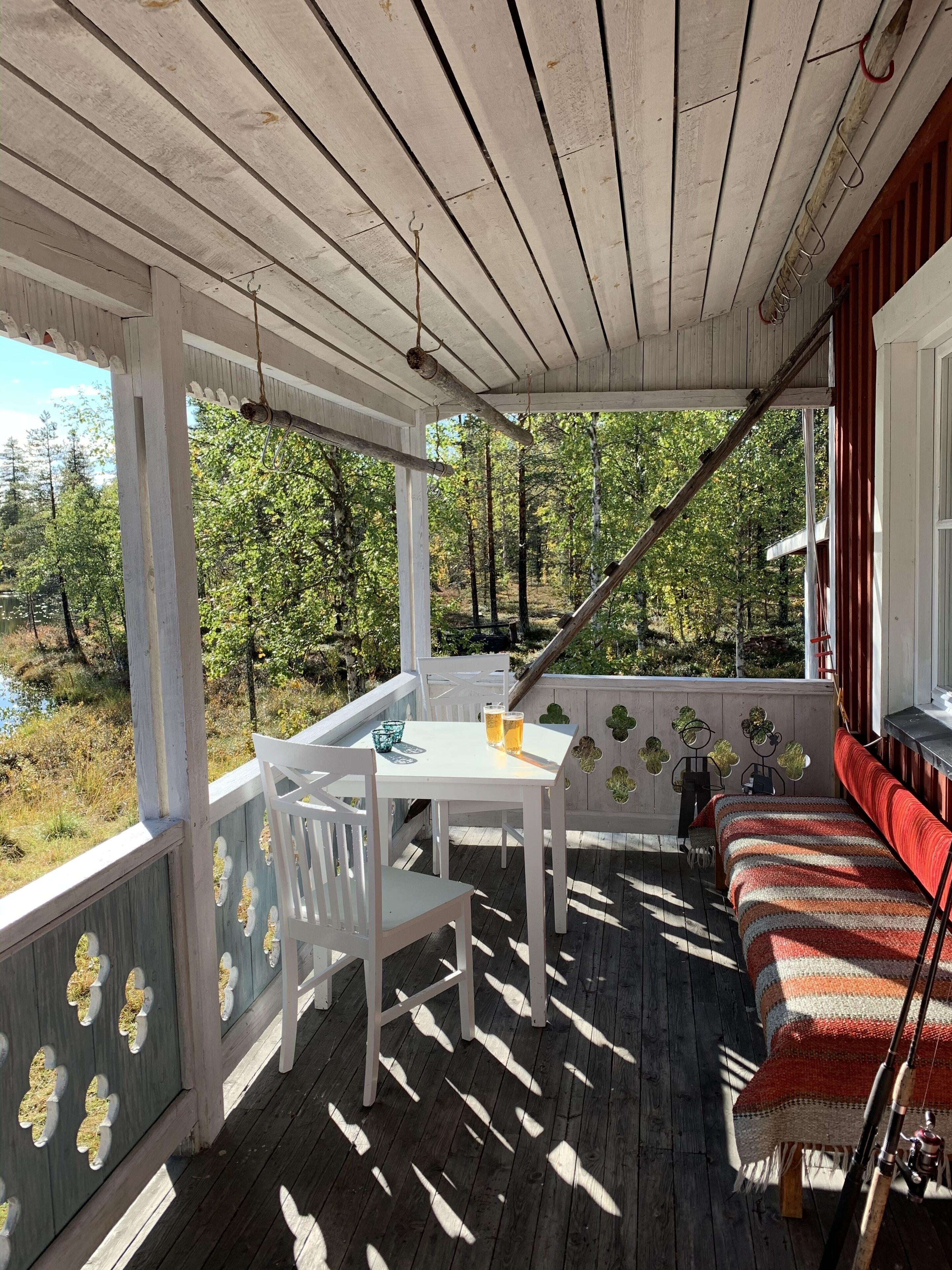 A covered porch with a table and chairs, a bench, and a view of a forested area.
