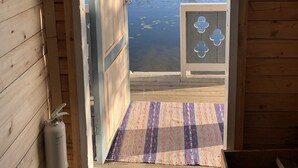 Une cabane en bois avec une porte donnant sur un quai surplombant un lac, le tout entouré d’arbres.