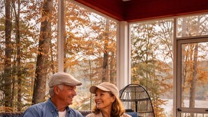 Un couple est assis sur un canapé bleu dans une pièce dotée de grandes fenêtres, d'une chaise en osier et d'une table sur laquelle se trouvent des verres et une bougie.