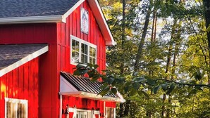 Une maison rouge avec un porche, des volets blancs et un petit jardin avec des chaises rouges.