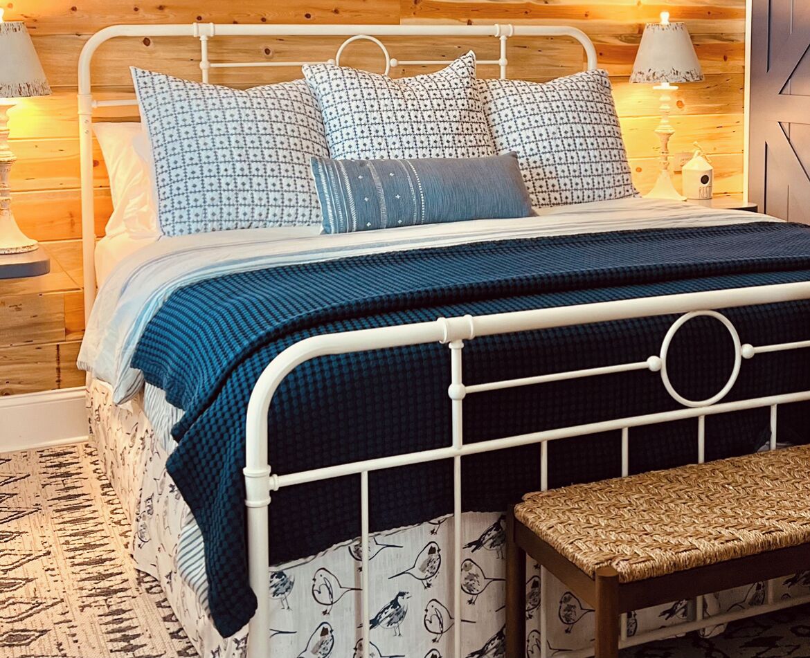 A bed with a white metal frame, blue bedding, and patterned pillows.