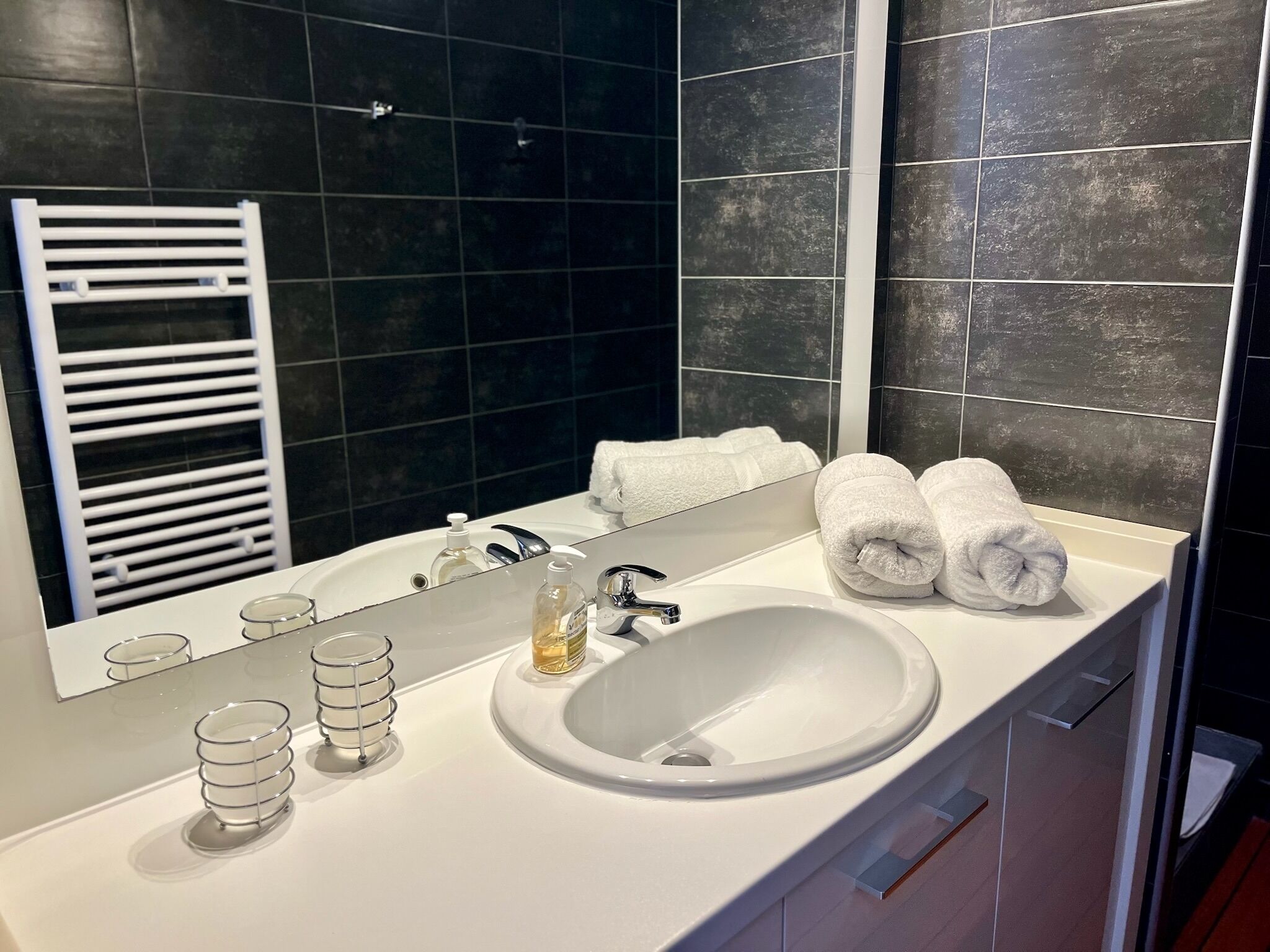 A modern bathroom with a white sink, a large mirror, and a towel rack.