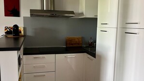 A modern kitchen with white cabinets, a black countertop, and a stainless steel range hood. - Alpilles-side apartment with terrace in Saint-Remy-de-Provence (Saint-Rémy-de-Provence)