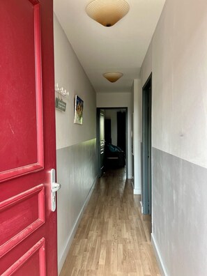 A hallway with a red door, wooden flooring, and a ceiling light fixture.
