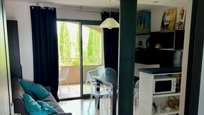 A modern living room with a grey sofa, a wooden bench, and a dining area with a table and chairs. There is a balcony with a view of greenery. - Alpilles-side apartment with terrace in Saint-Remy-de-Provence (Saint-Rémy-de-Provence)