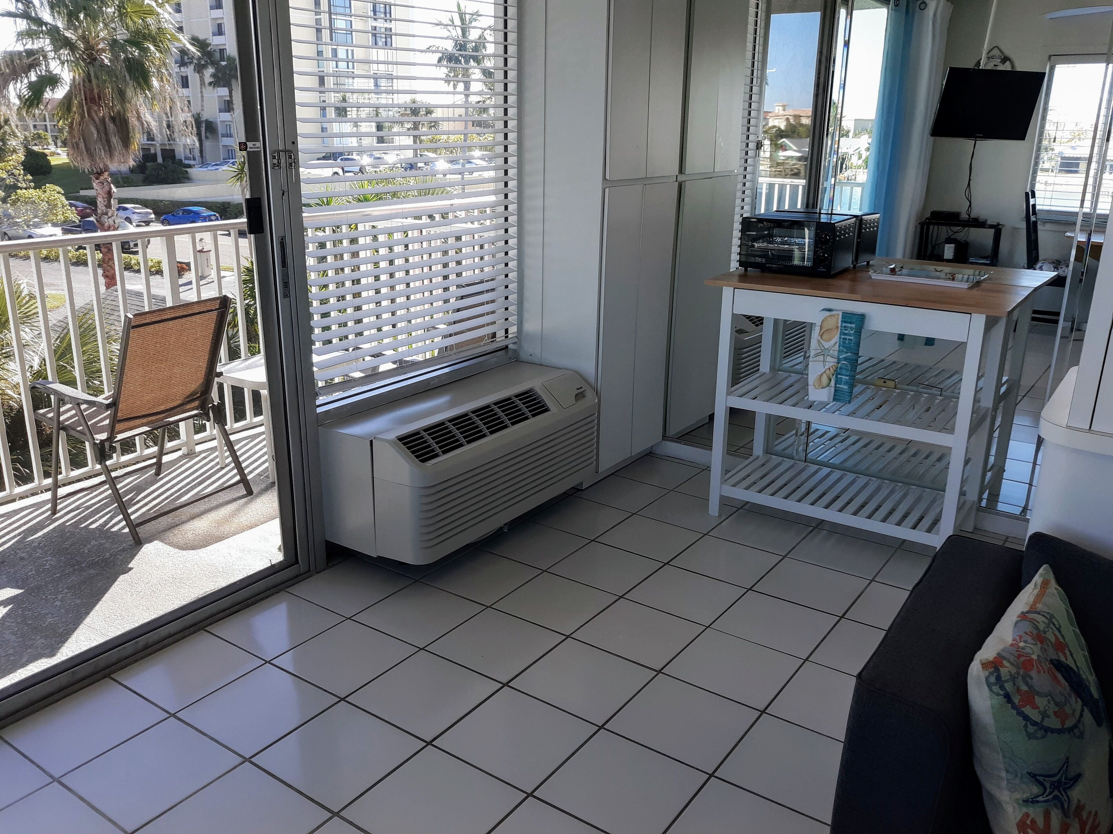 Un balcón con una silla, un aire acondicionado blanco y una mesa blanca con estantes.