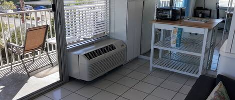 Un balcón con una silla, un aire acondicionado blanco y una mesa blanca con estantes.