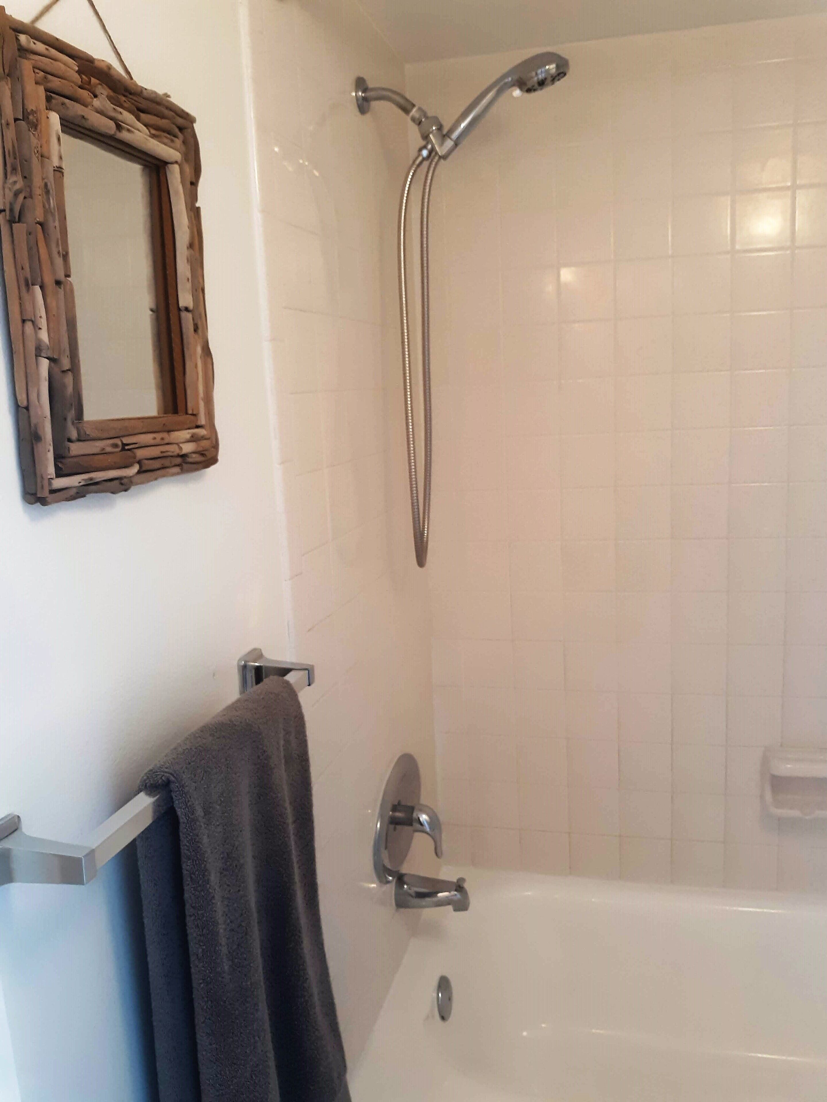 A bathroom with a white tiled shower, a wooden-framed mirror, and a towel rack.