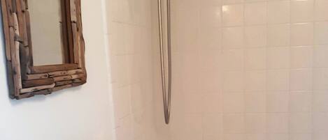 A bathroom with a white tiled shower, a wooden-framed mirror, and a towel rack.