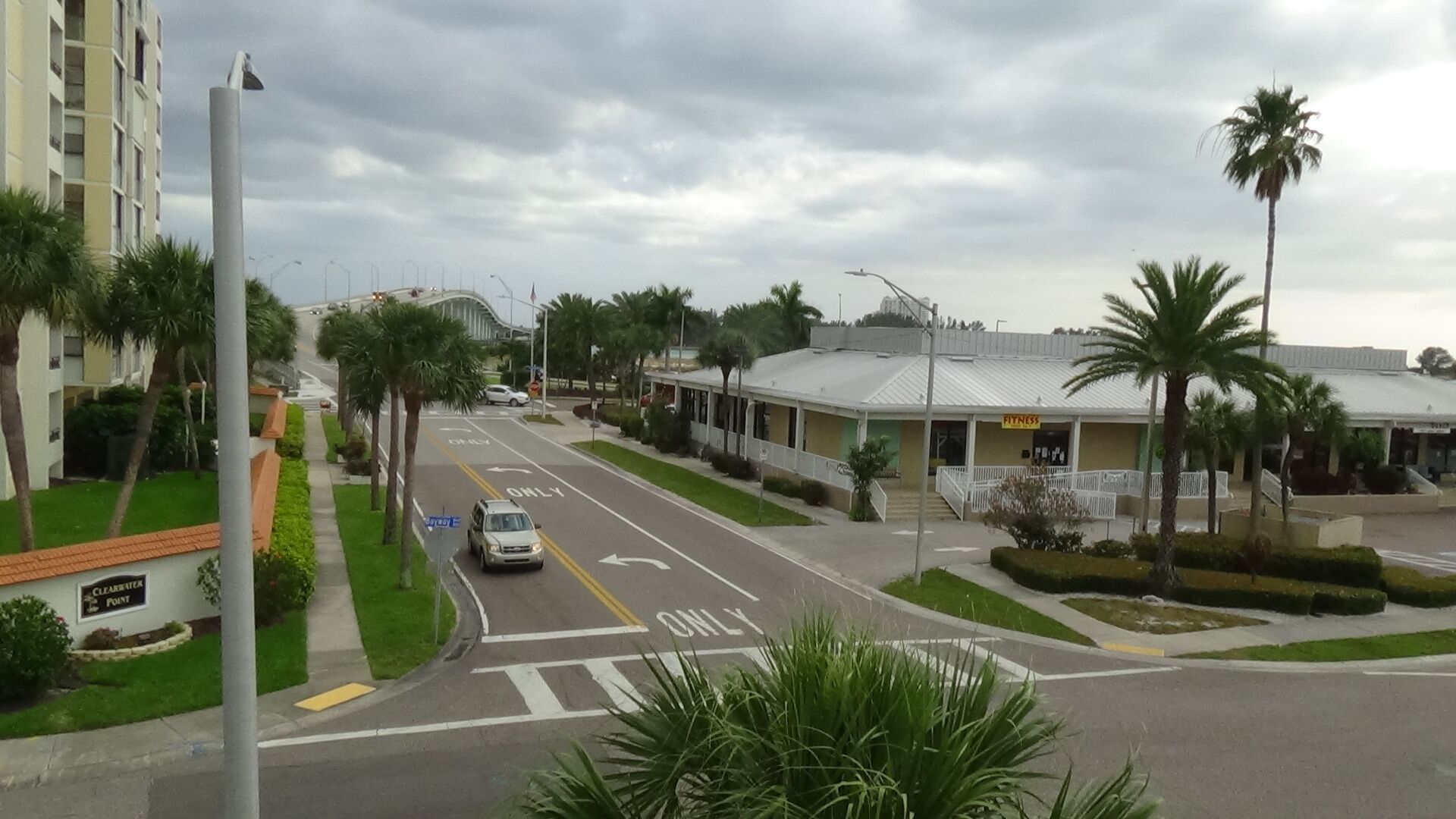 A street view with a fitness center, palm trees, and a building with a sign.