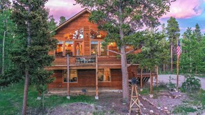A two-story wooden cabin with a balcony, surrounded by trees.