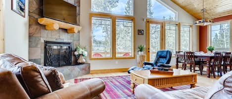 A spacious living room with leather sofas, a fireplace, large windows, and a dining area.