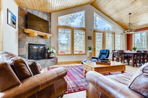 A spacious living room with leather sofas, a fireplace, large windows, and a dining area.